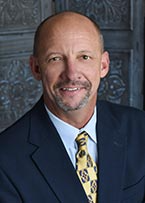A man in a blue shirt and tie is smiling for the camera.