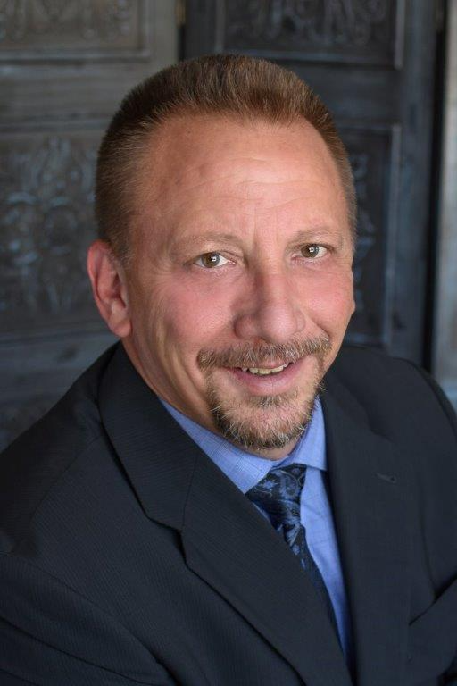 A man in a blue shirt and tie is smiling for the camera.