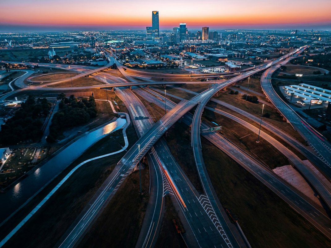 An aerial view of a highway intersection at night with a city in the background.