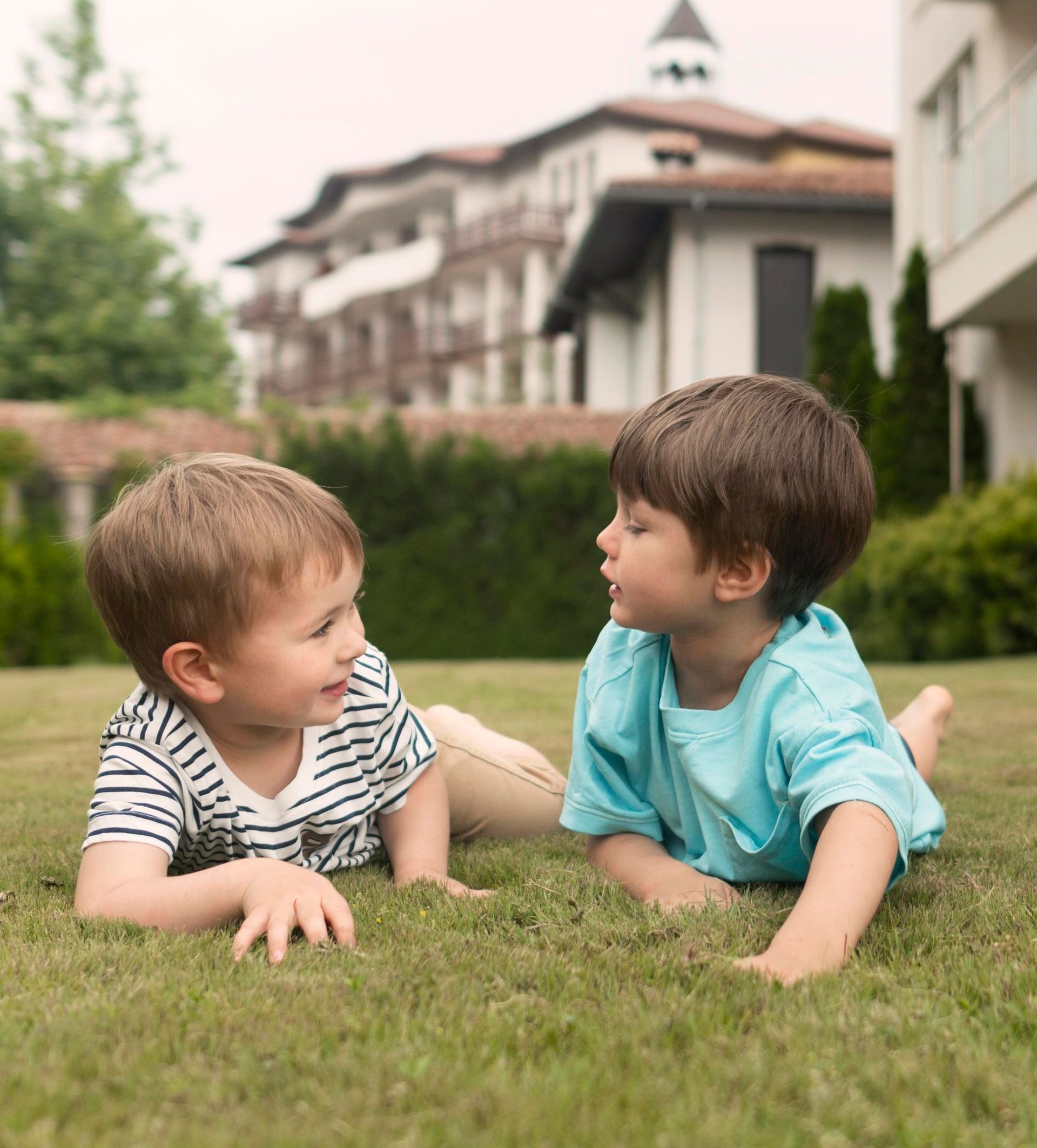 Two young boys are laying on the grass and talking to each other.