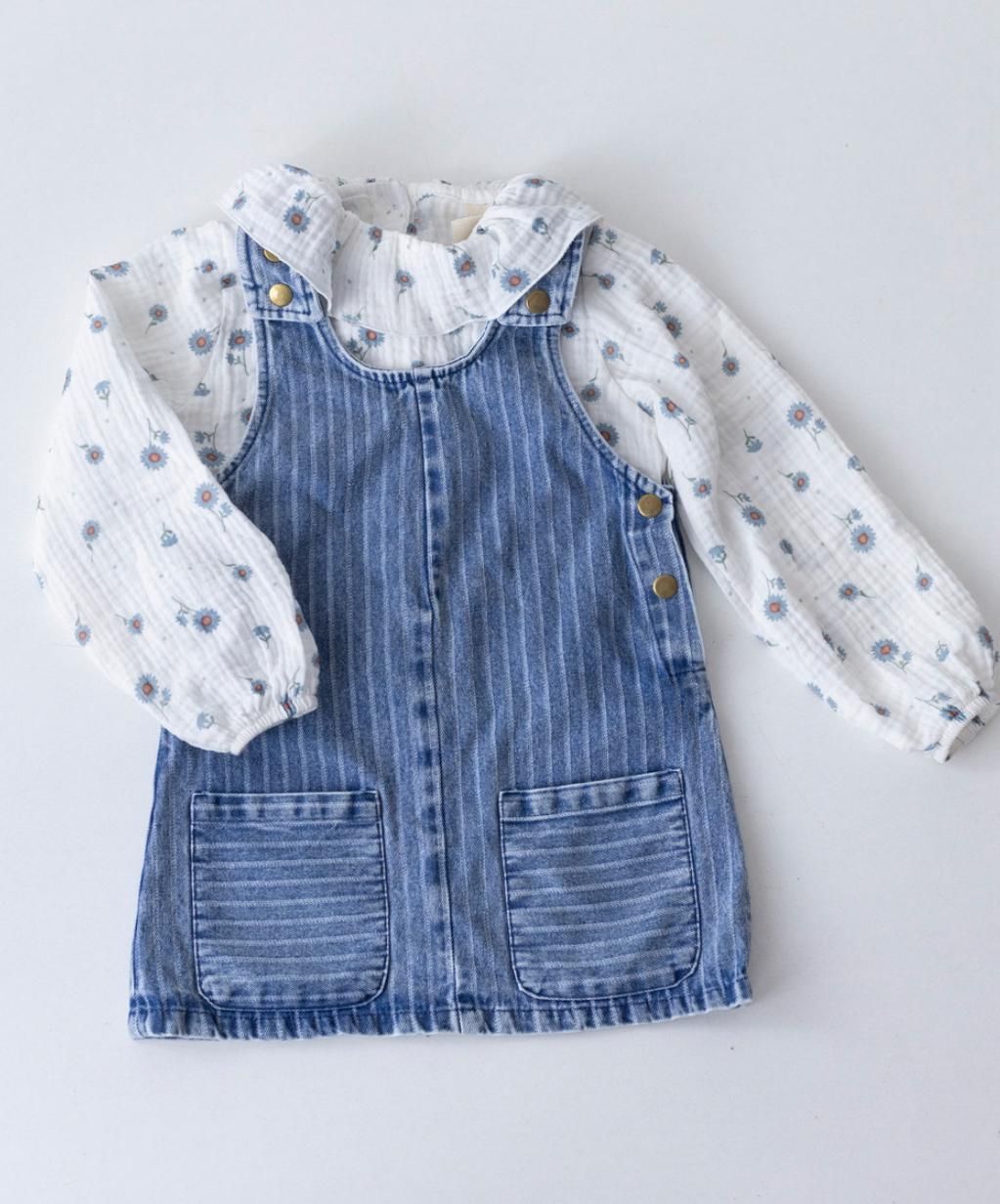 Una niña lleva un vestido de mezclilla y una camisa blanca.