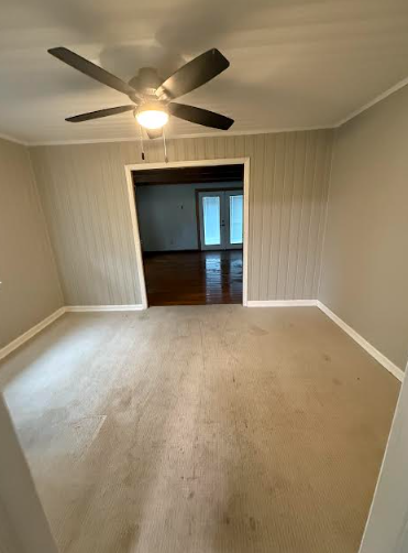 Empty room with stained carpet, light gray walls, ceiling fan. View through doorway to another room.