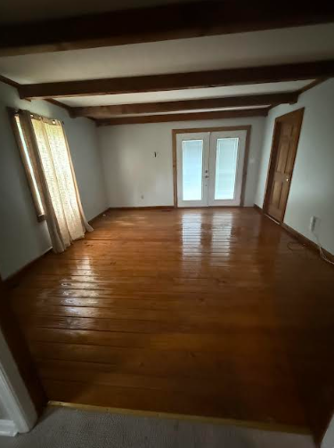 Empty room with wood floors, white walls, exposed wood beams, and double doors.