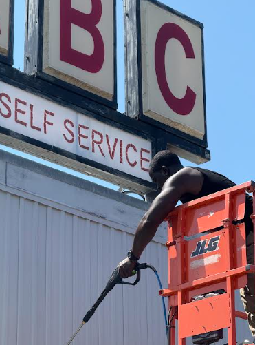 Man on a lift pressure washing a building sign that reads