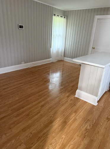 Empty room with wood floors, paneled gray walls, white trim, and a white cabinet.