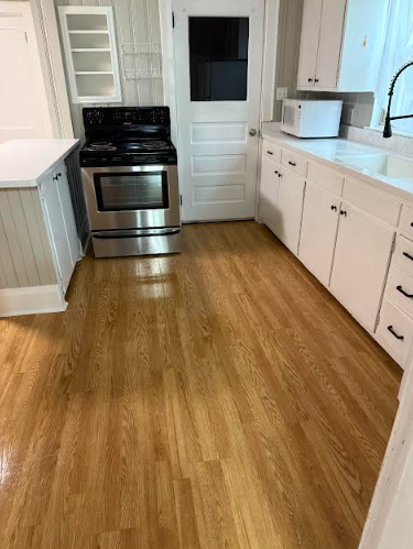 Kitchen with wood floors, white cabinets, stainless steel oven, and a white microwave.