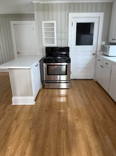 Kitchen with a white island and cabinets, a stainless steel oven, and wood flooring.
