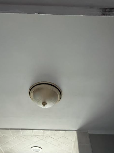 White ceiling with a circular light fixture; corner of a tiled wall visible.