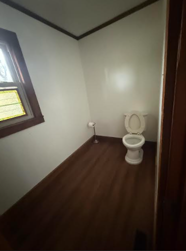 Small bathroom with a white toilet, brown trim, and a window on the left.