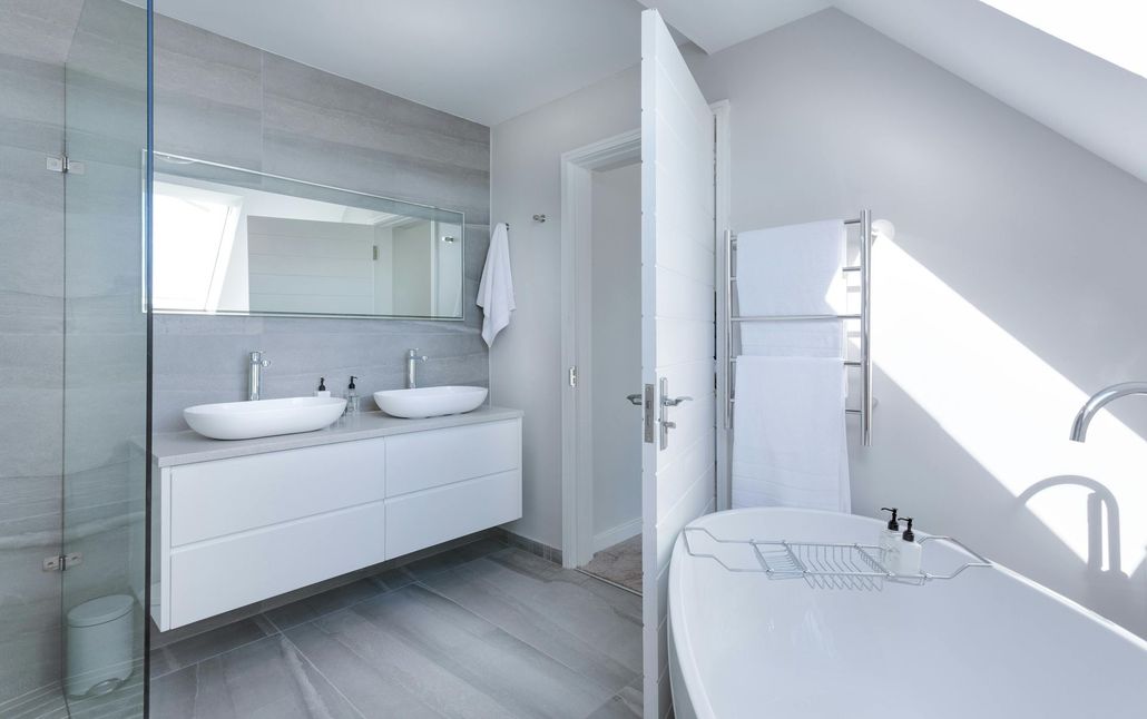 Modern white bathroom with double sinks, bathtub, and a towel warmer.