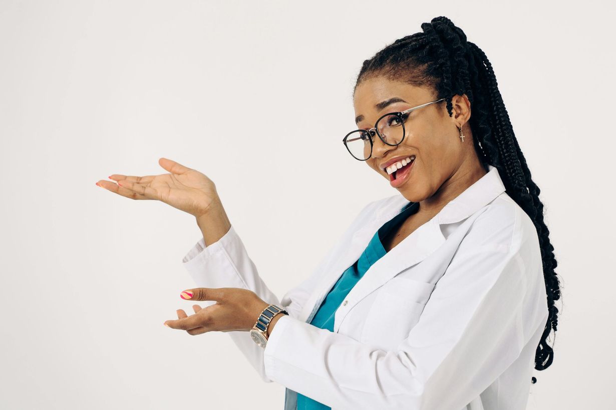 Smiling doctor in white coat and glasses presenting with open hands on a light background