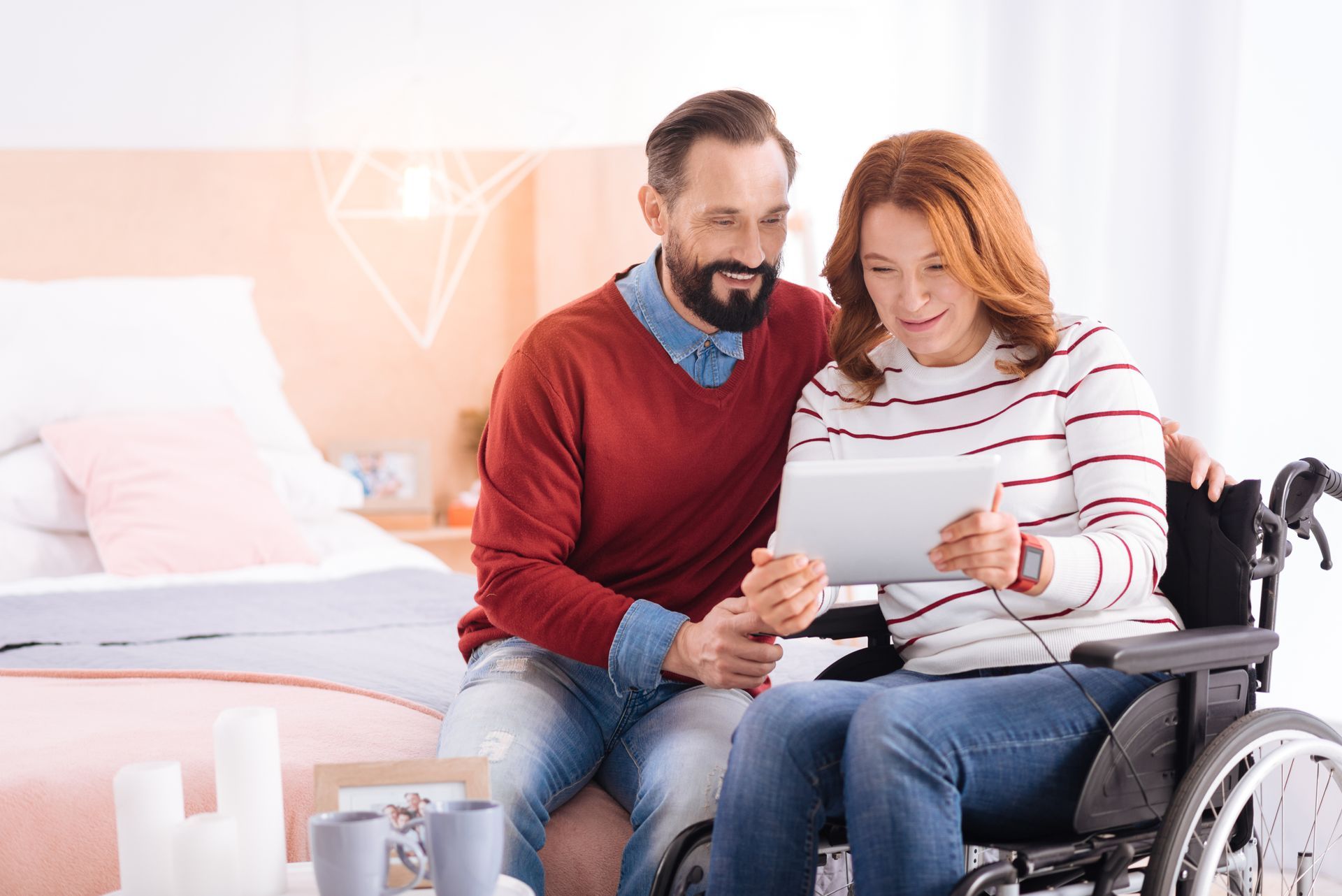 A man is sitting next to a woman in a wheelchair looking at a tablet.