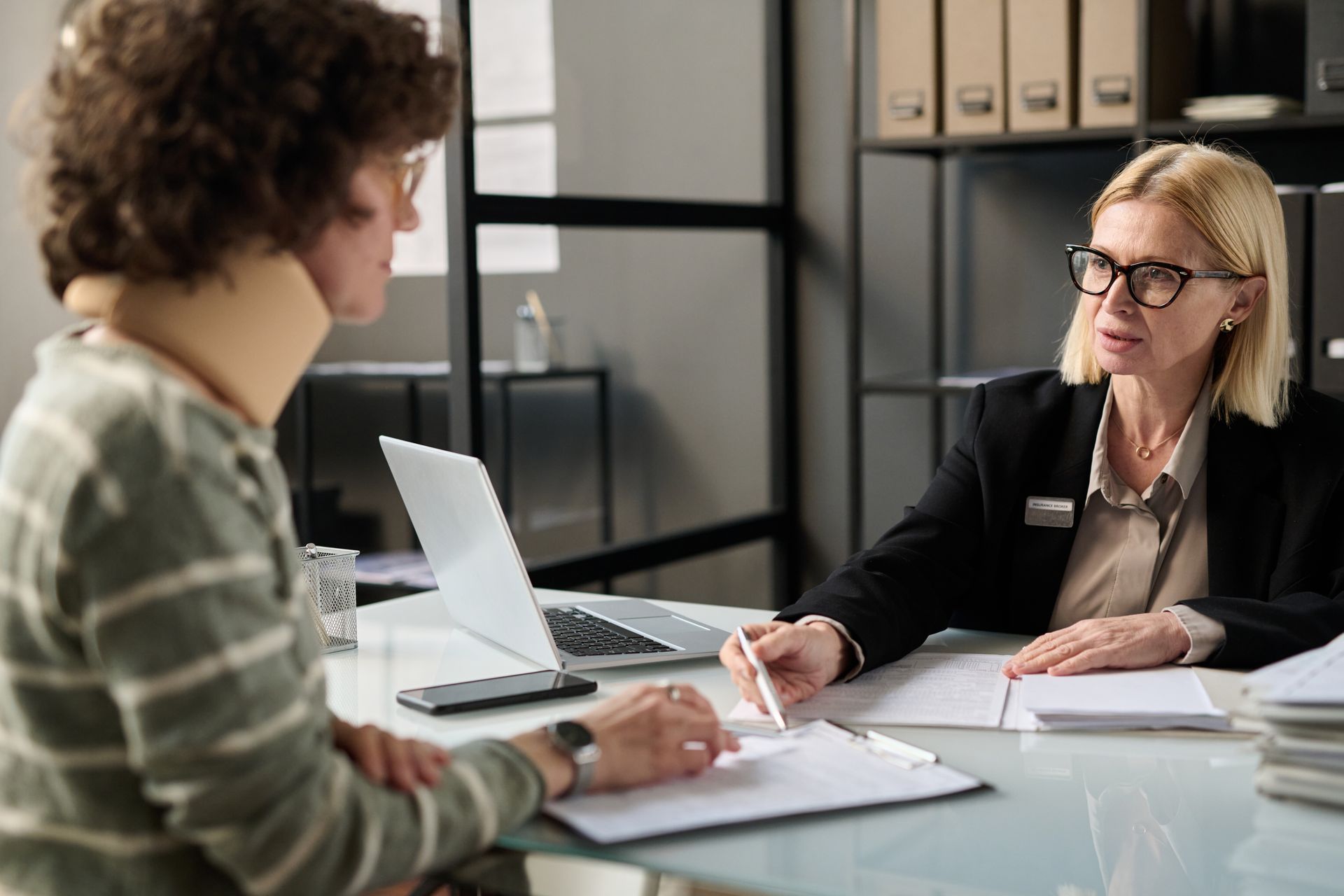 A woman is sitting at a table talking to a man with a neck brace.
