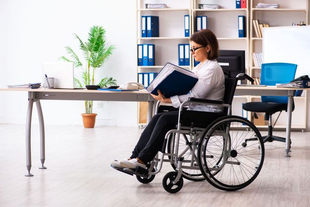 A woman in a wheelchair is reading a book in an office.