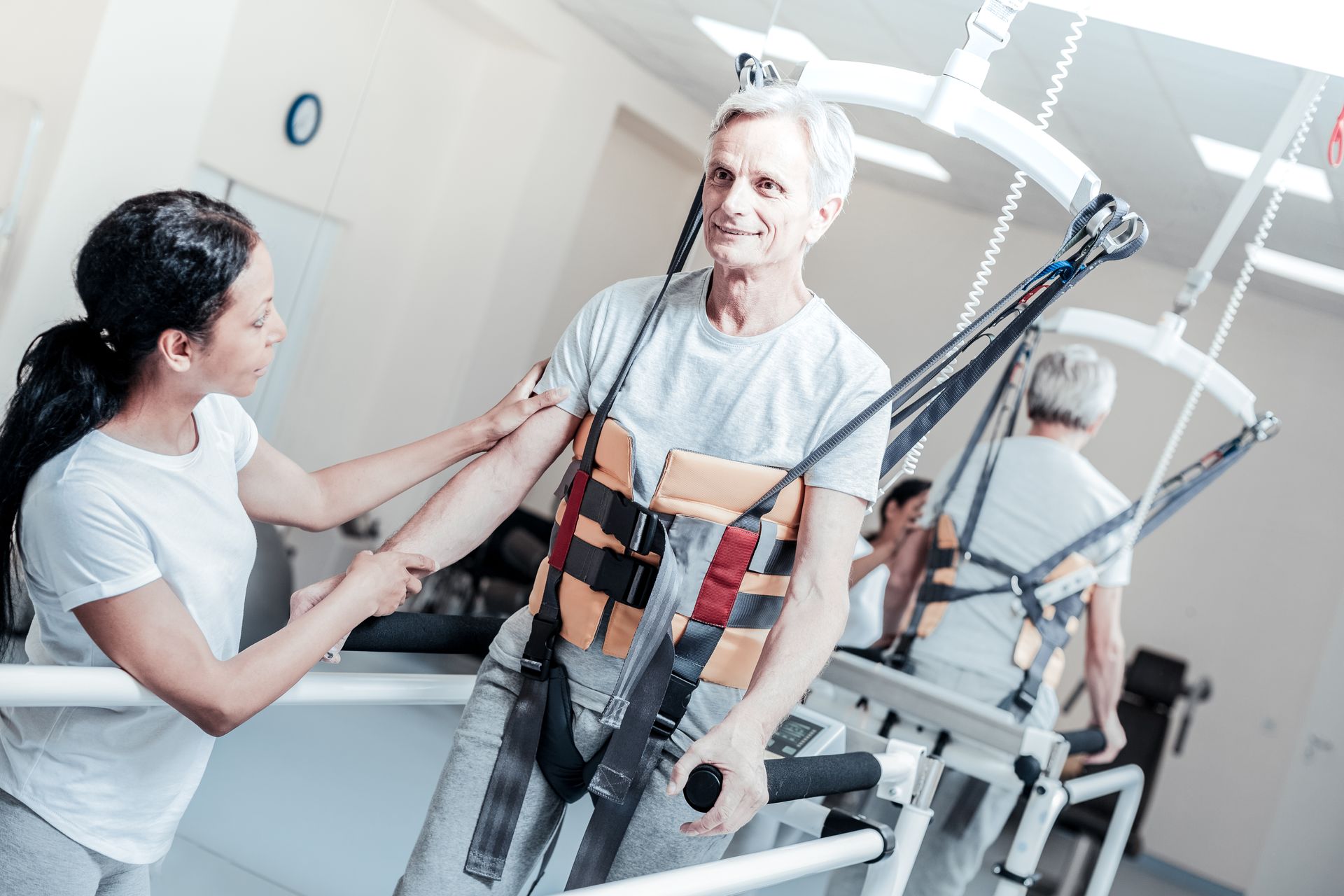 A woman is helping an elderly man walk on a treadmill.