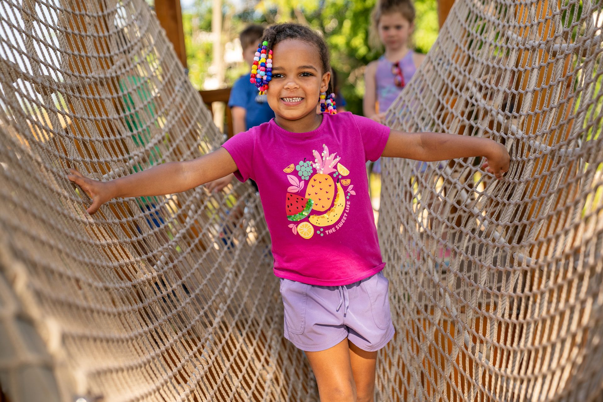 A little girl is standing in a hammock with her arms outstretched.