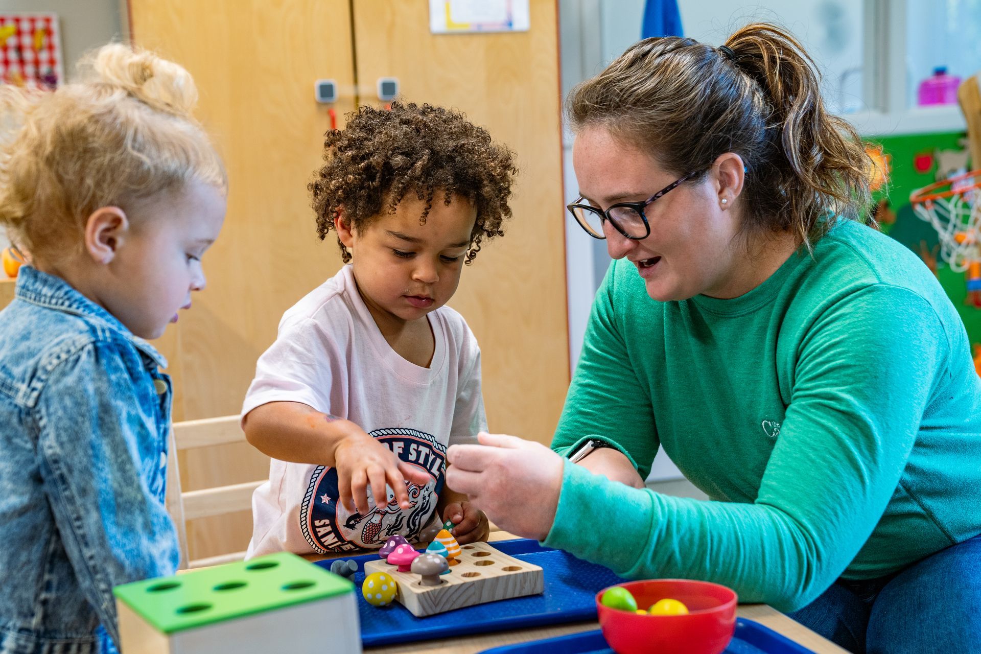 A woman is playing with two young children at a table.