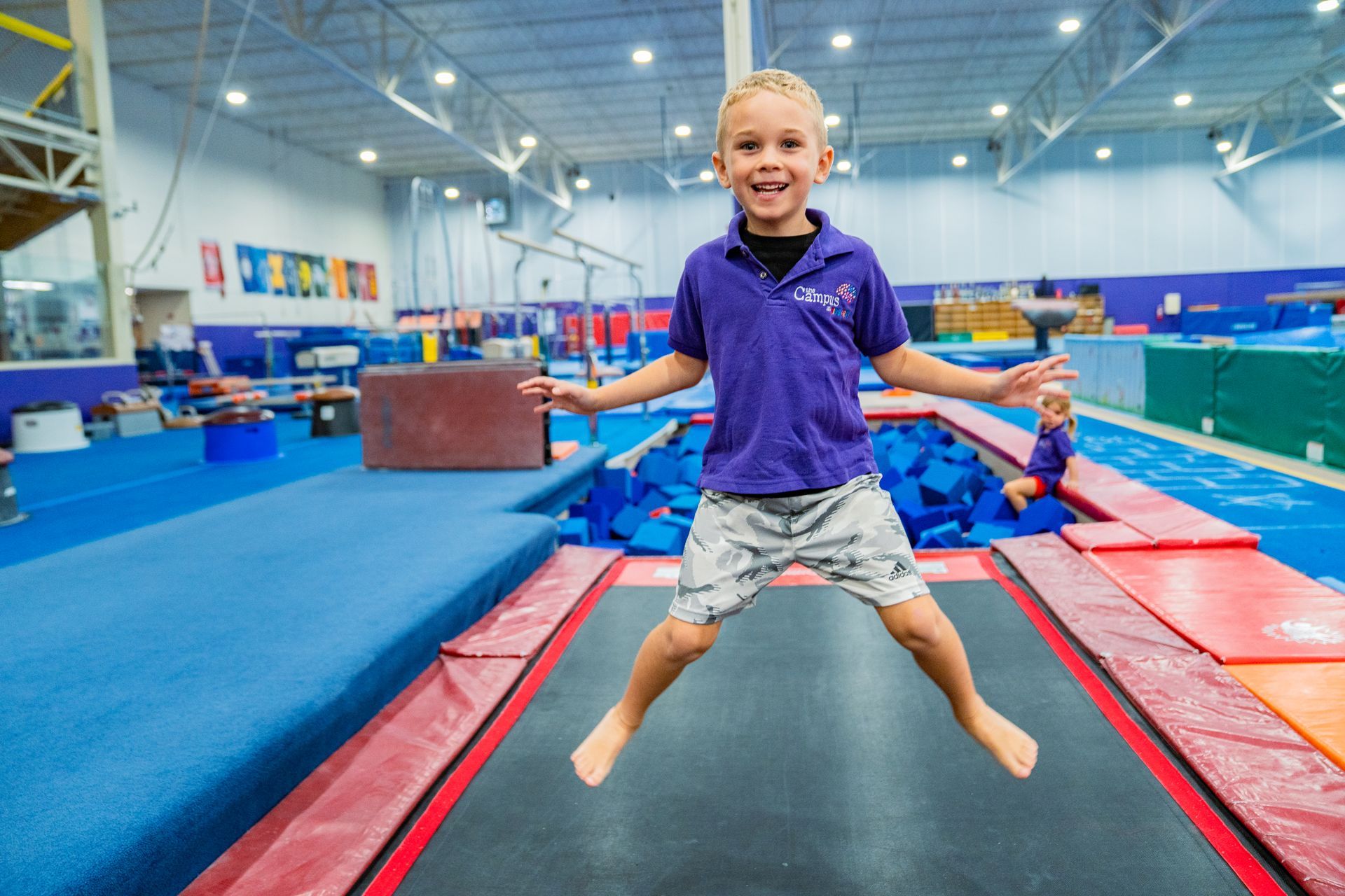 A young boy is jumping on a trampoline in a gym.