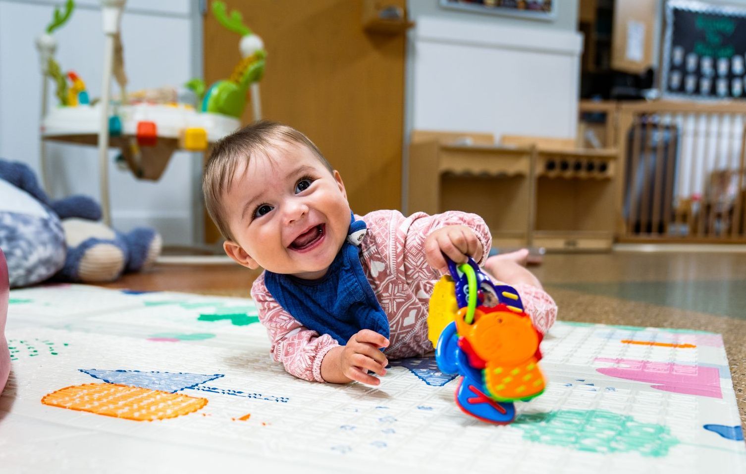 A baby is playing with a toy on the floor and smiling.