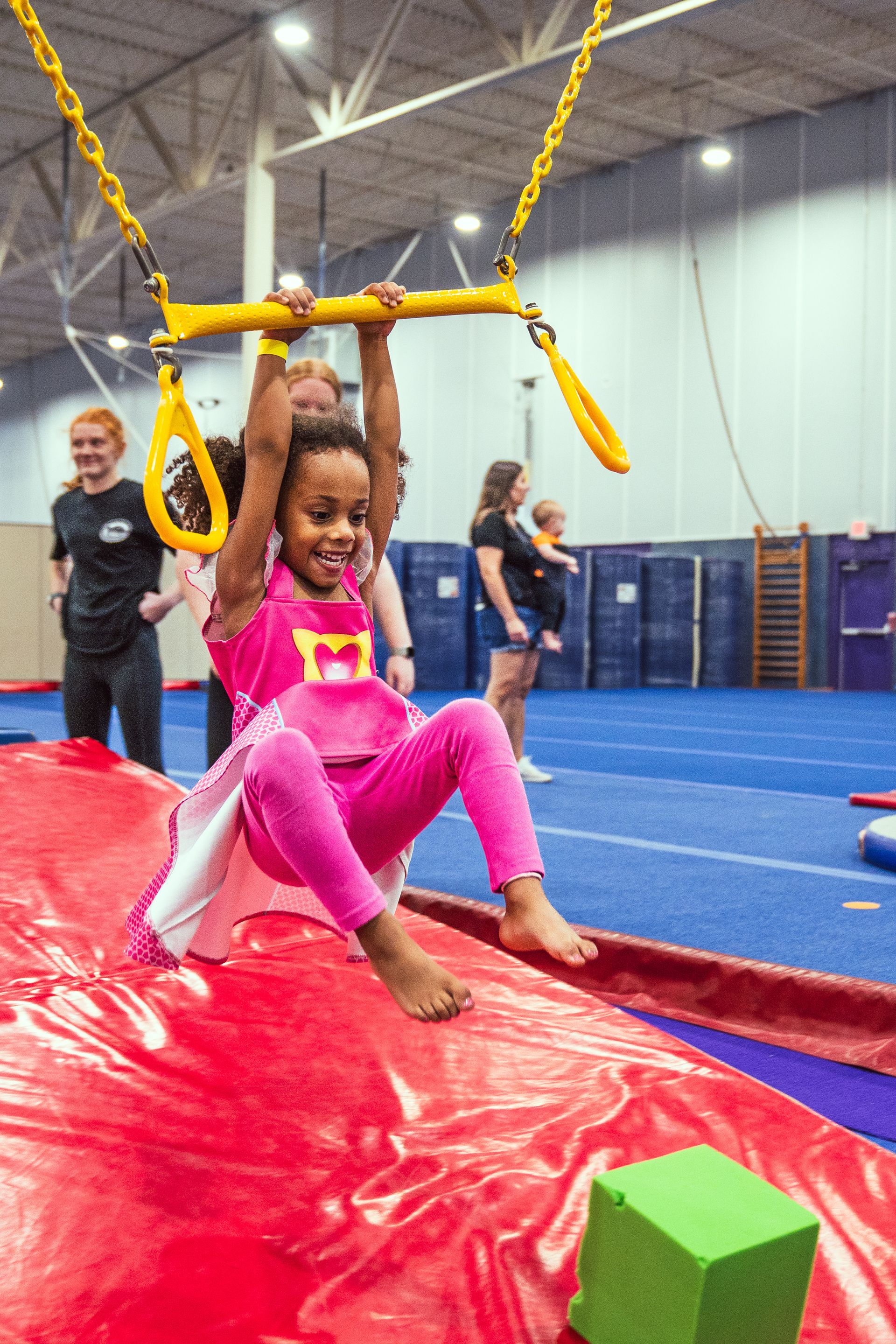 A little girl is sitting on a balance beam in a gym.