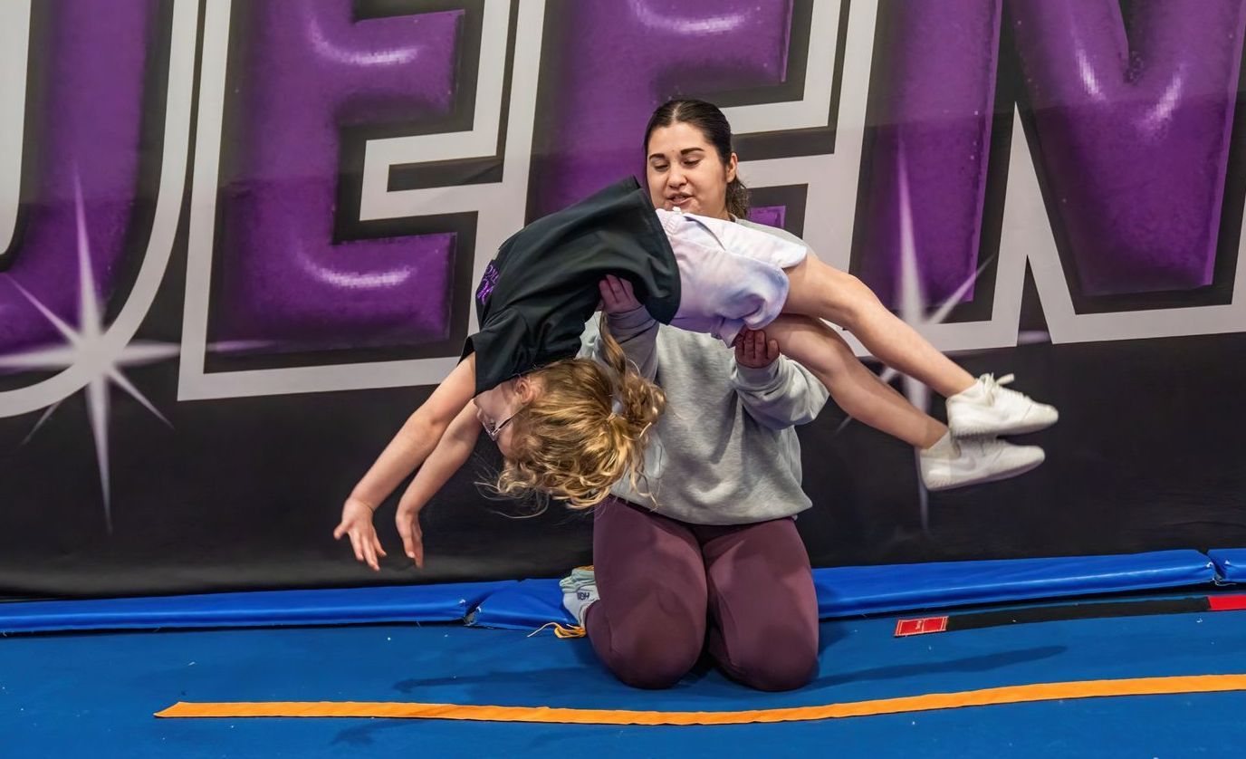 A woman is kneeling down next to a child on a trampoline.