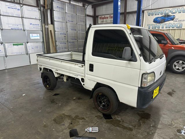 Small white flatbed mini truck parked indoors in a garage or workshop, with black wheels and a yellow front plate.