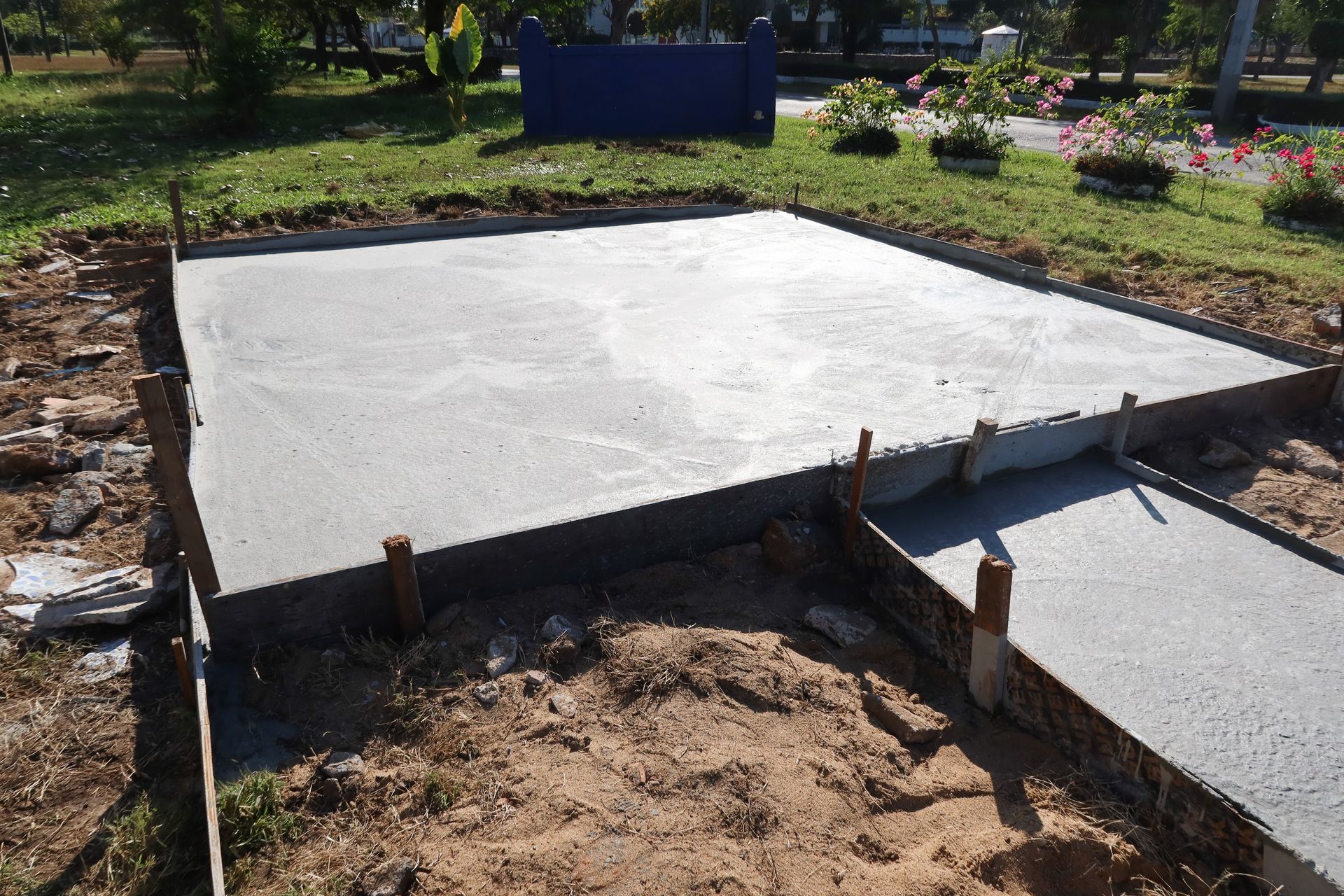 Une dalle de béton fraîchement coulée et une extension de passerelle, le tout entouré de coffrages en bois, sur un terrain herbeux.