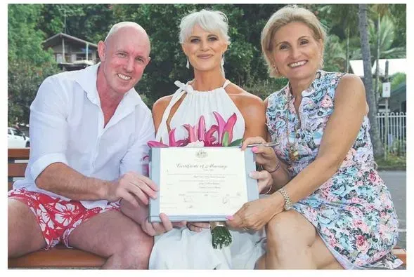 A Man and Two Women Are Sitting on a Bench Holding a Certificate — GinaS Cairns Tropical Weddings in Parramatta Park, QLD