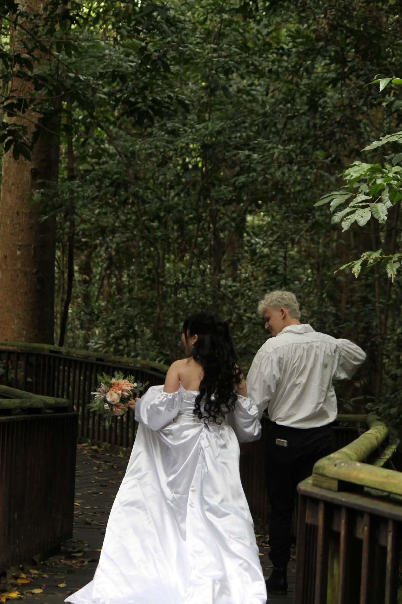 Two people in formal attire walking along a wooded boardwalk — GinaS Cairns Tropical Weddings in Parramatta Park, QLD