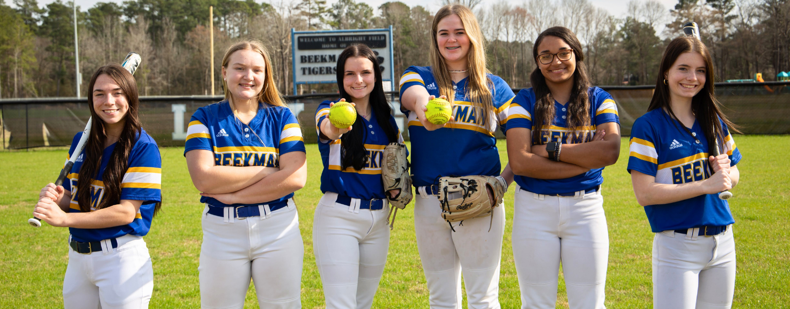 A group of softball players are posing for a picture on a field.