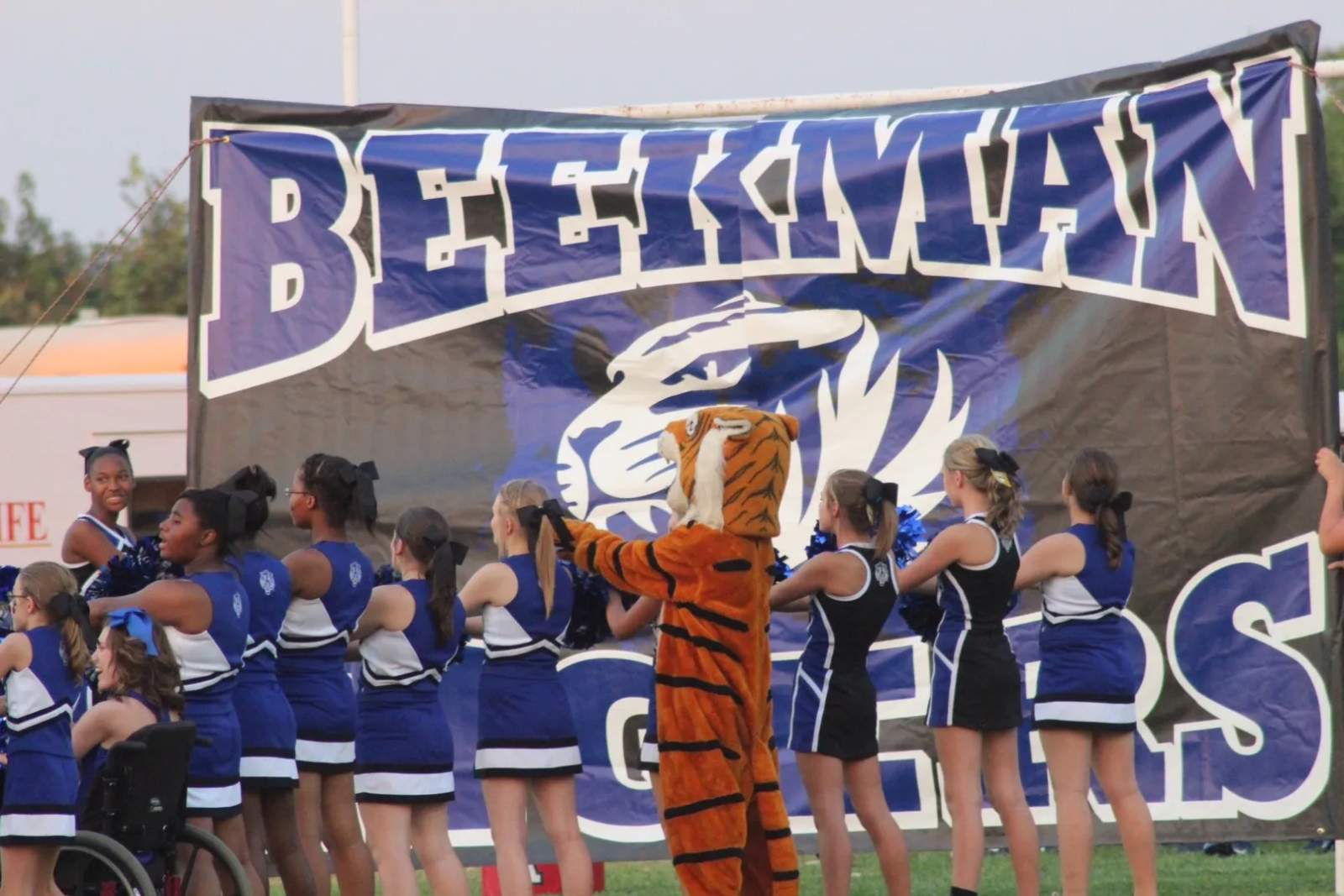 A group of cheerleaders are standing in front of a beckman banner