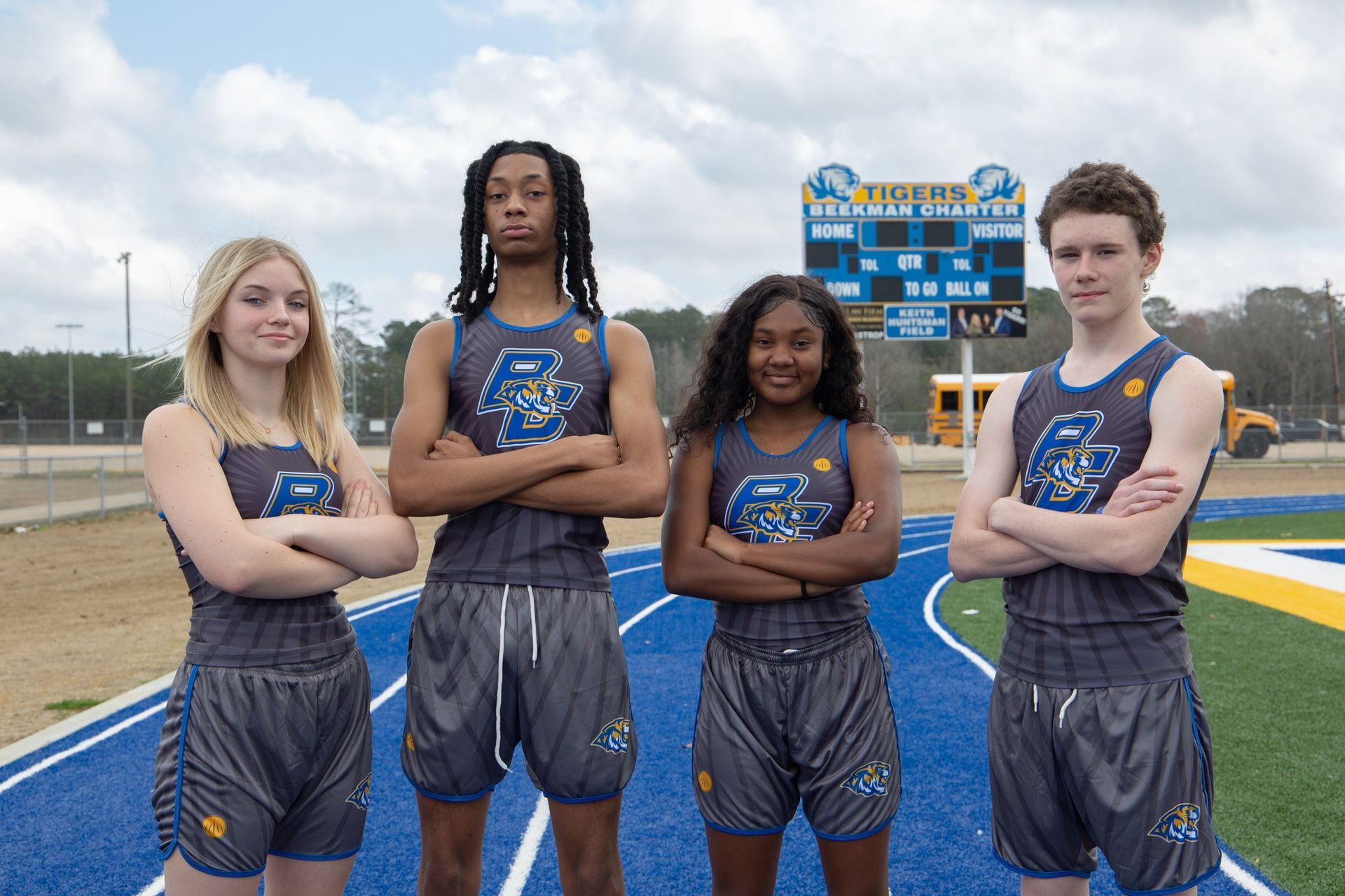 A group of young people standing on a track with their arms crossed.