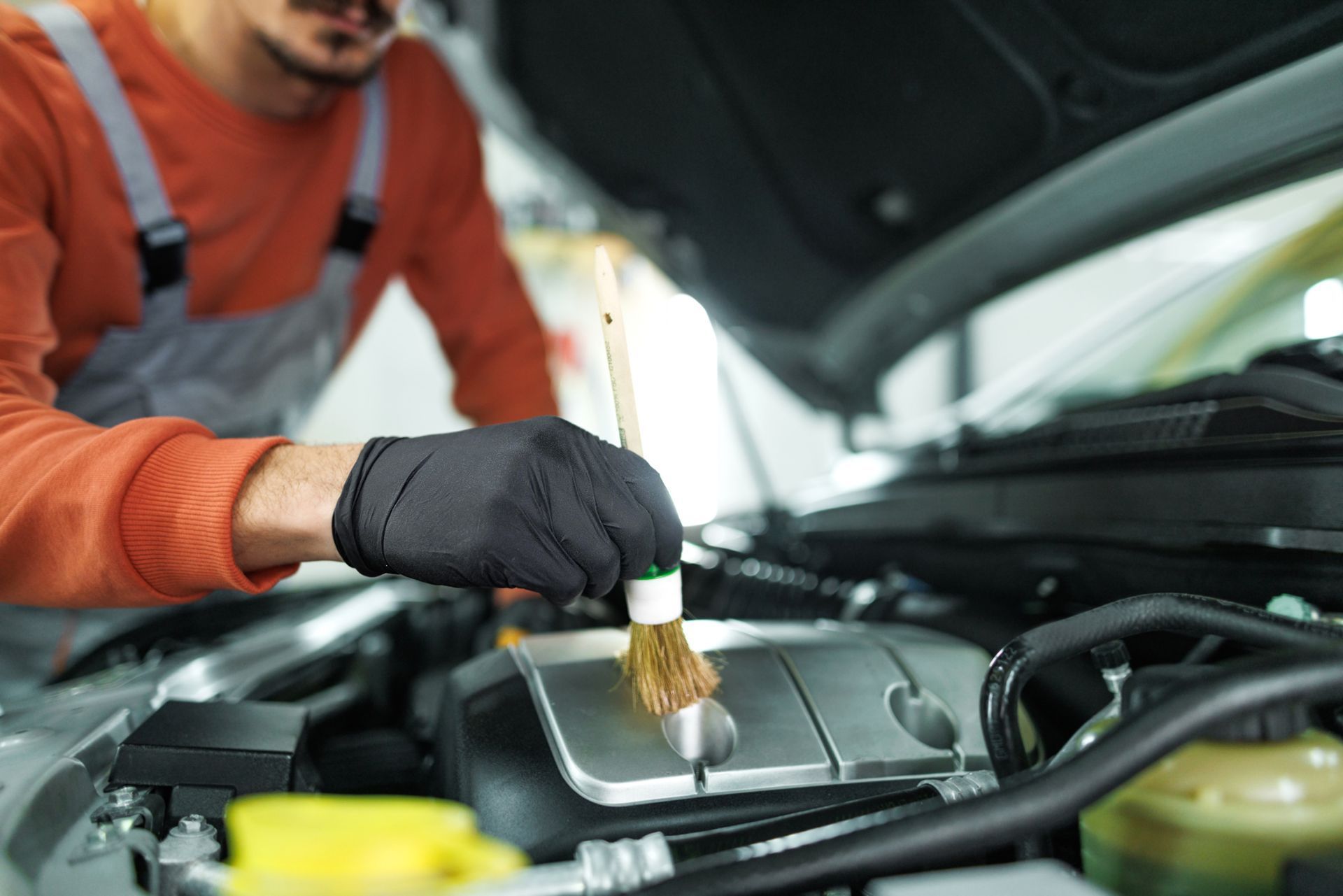 A man is cleaning the engine of a car with a brush.