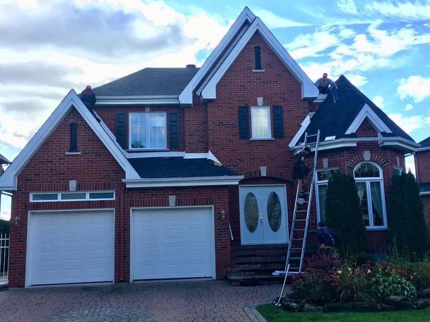 A man is standing on a ladder in front of a large brick house.