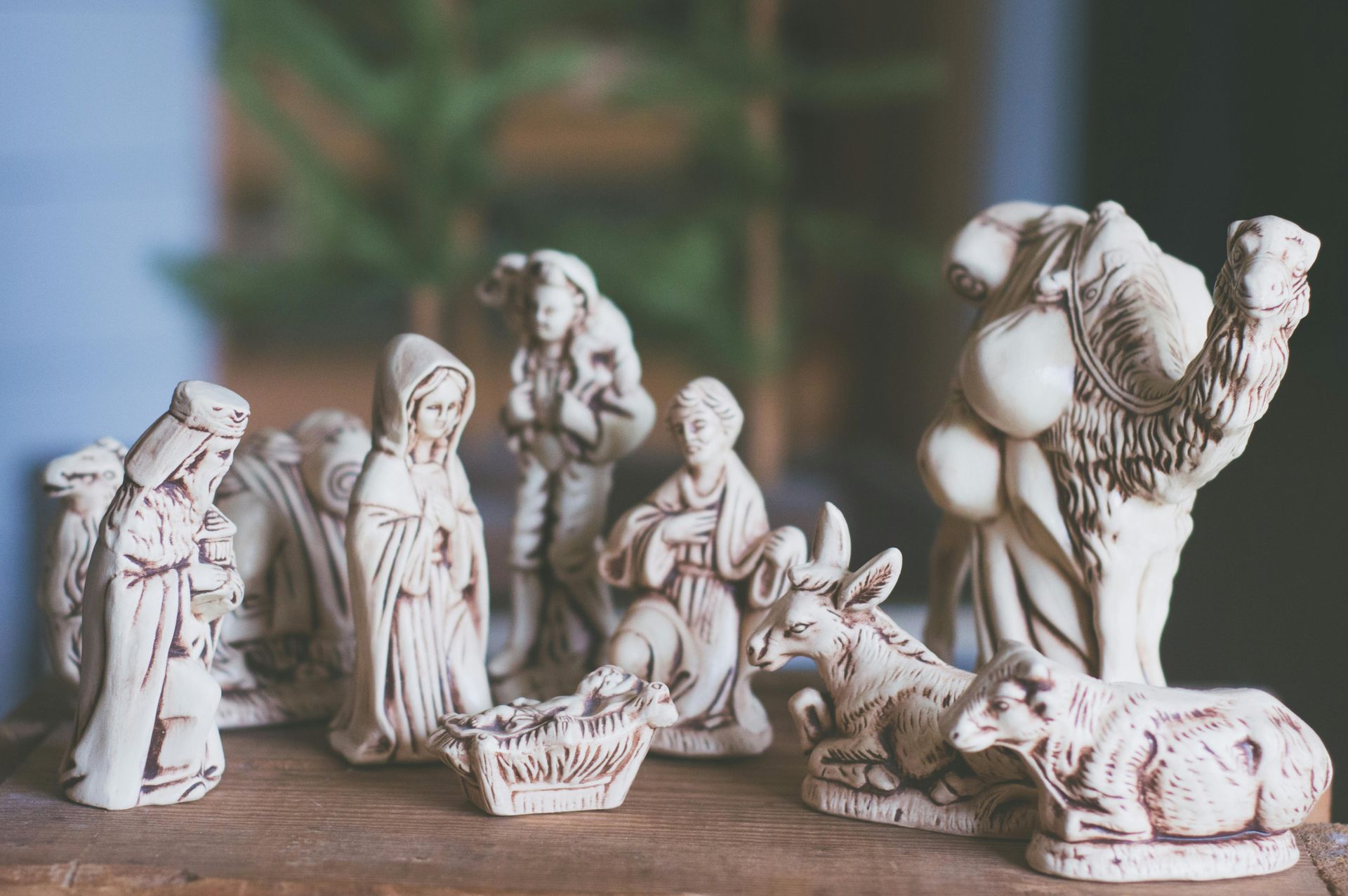 Nativity scene figurines on a wooden surface, including Mary, Joseph, animals, and a camel.