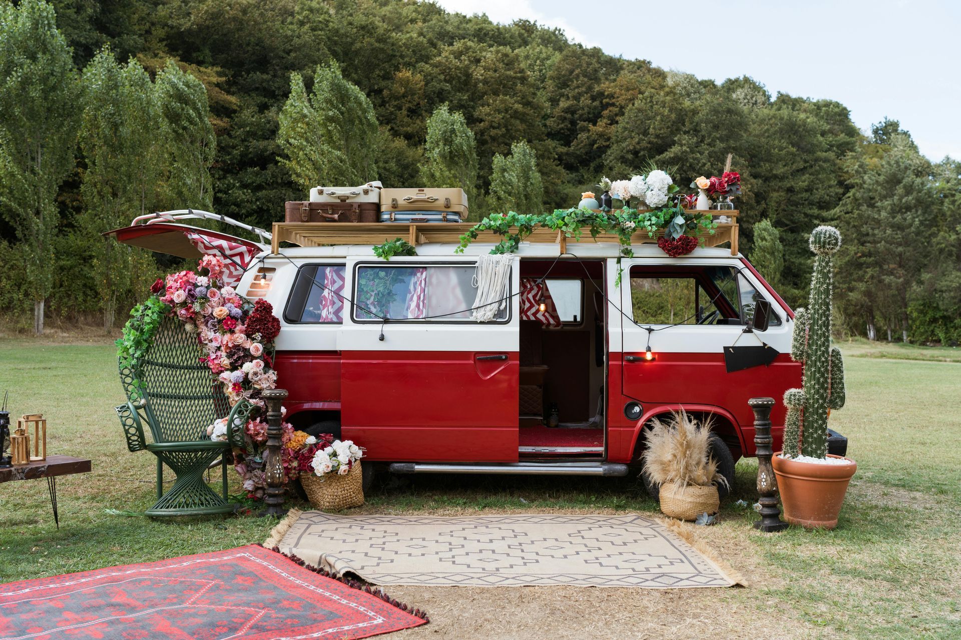 A red and white van decorated with flowers and cactus is parked in a field.