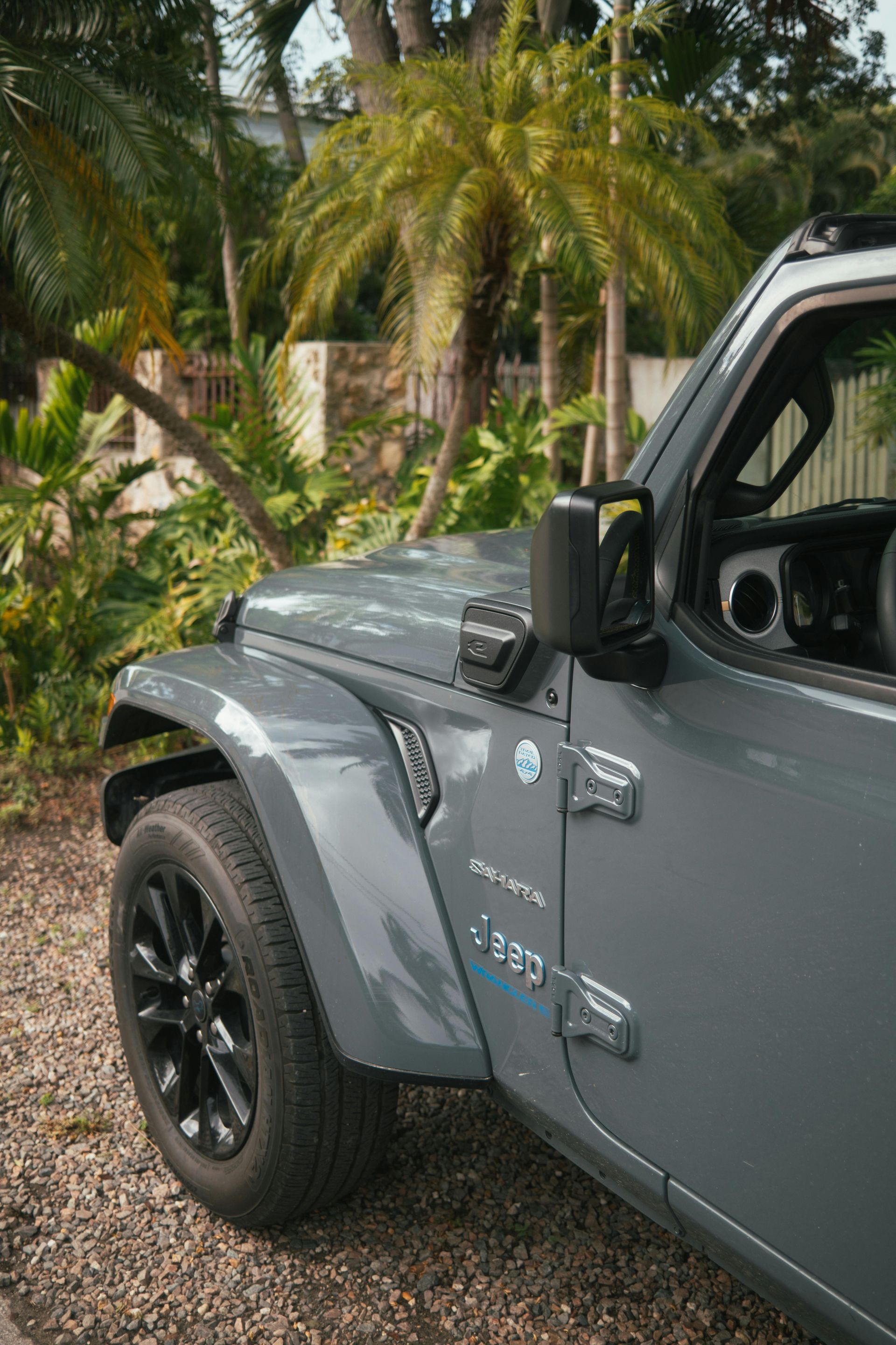 A jeep is parked in a gravel driveway next to trees.