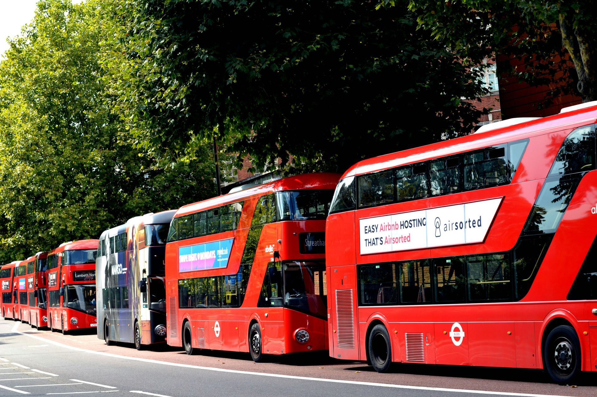 A row of red double decker buses parked on the side of the road