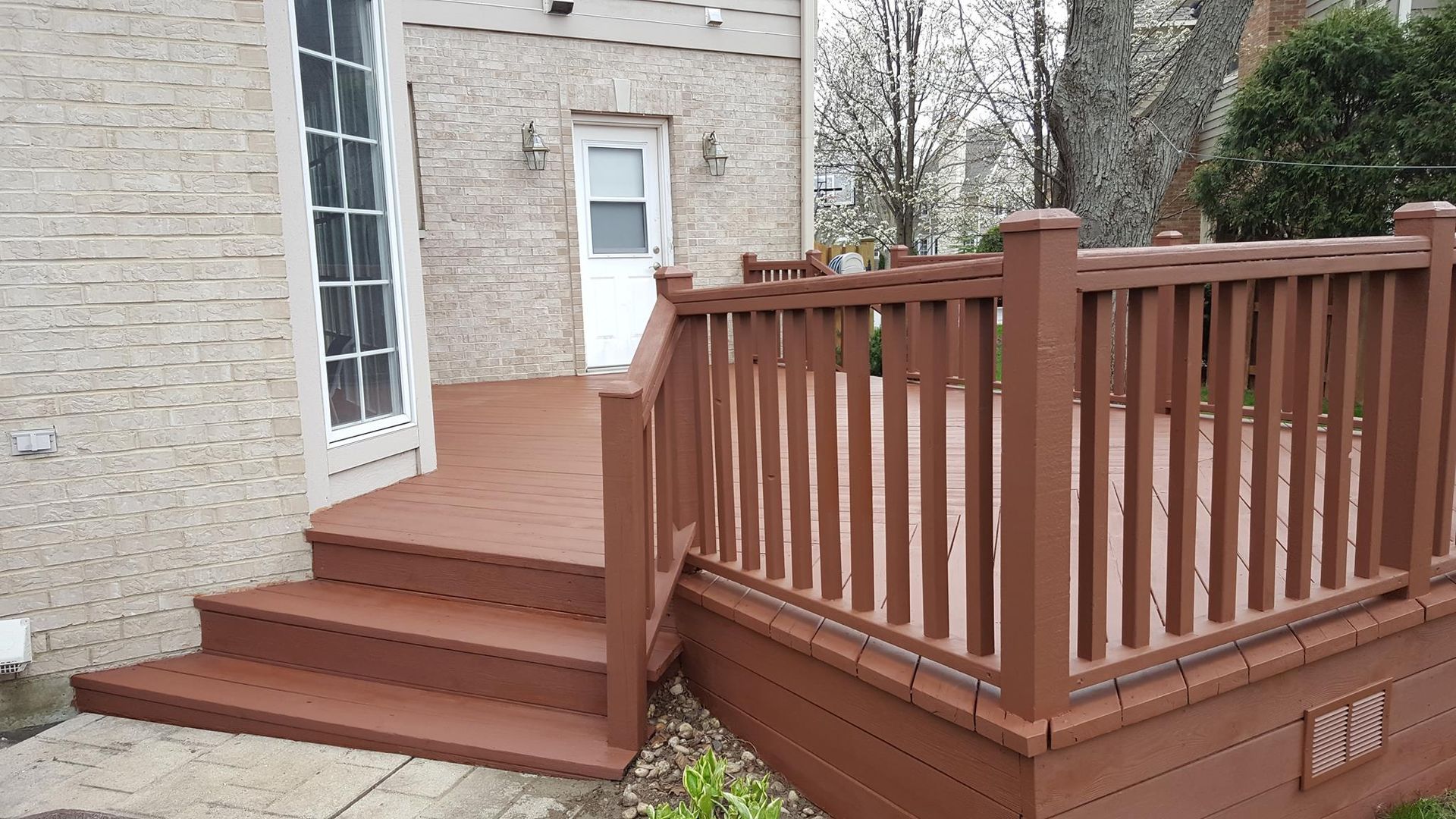 A wooden deck with stairs and a railing in front of a brick house.