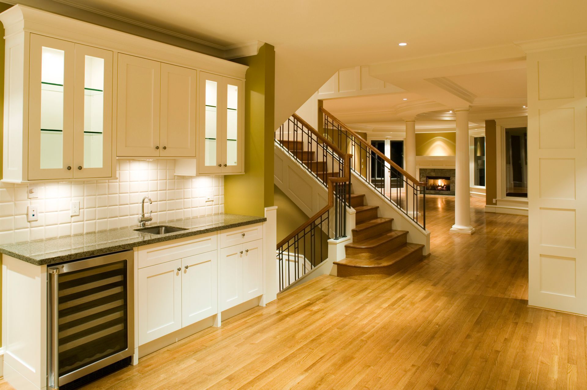 A kitchen with hardwood floors and white cabinets and a staircase.
