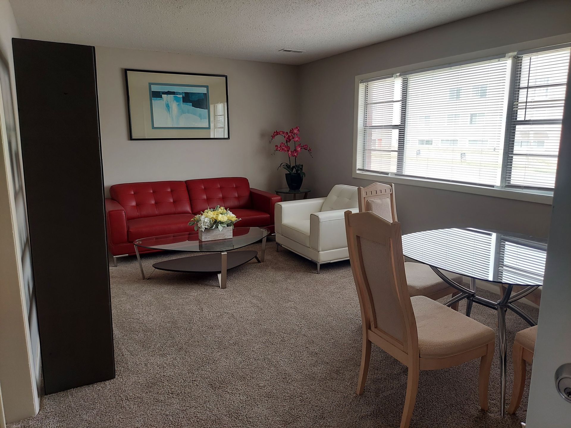 Living room with red sofa, white chair, round table, window, and artwork.