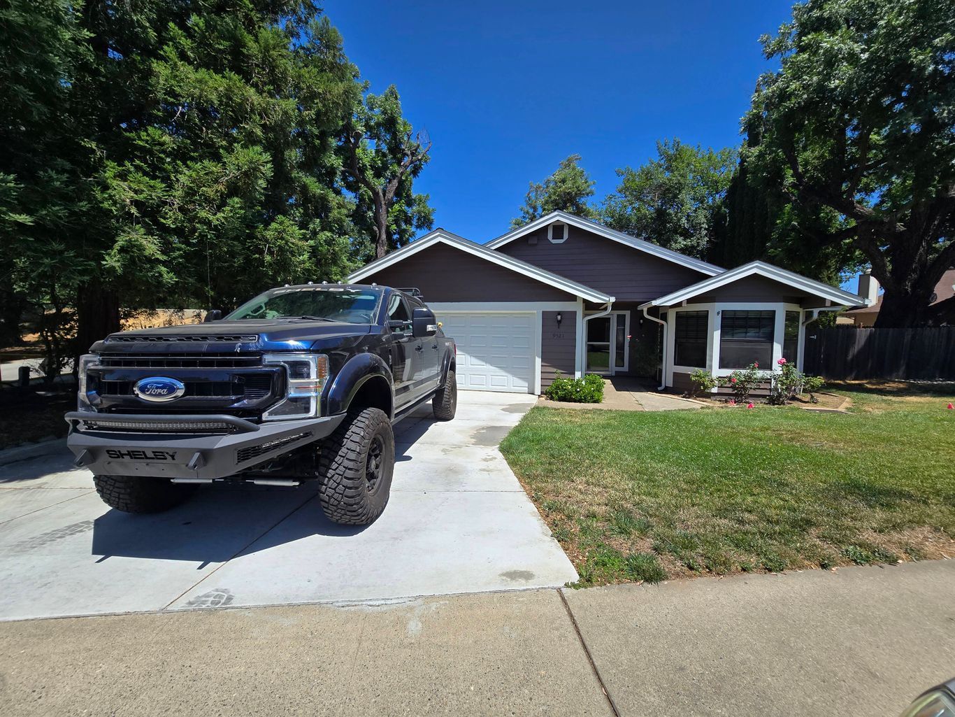 A dark blue Ford truck with a heavy-duty front bumper parked in the driveway of a single-story house.
