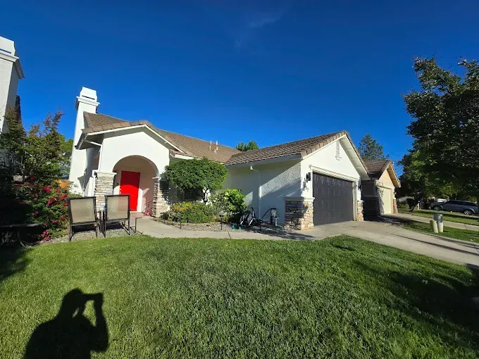 A single-story white house with a red front door, a black garage door, and stone accents under a clear blue sky.