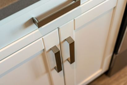 White kitchen cabinets with matte bronze rectangular handles and a matching horizontal drawer pull.