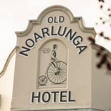 Sign for the Old Noarlunga Hotel, featuring a large-wheeled bicycle illustration and text against a cream-colored building.