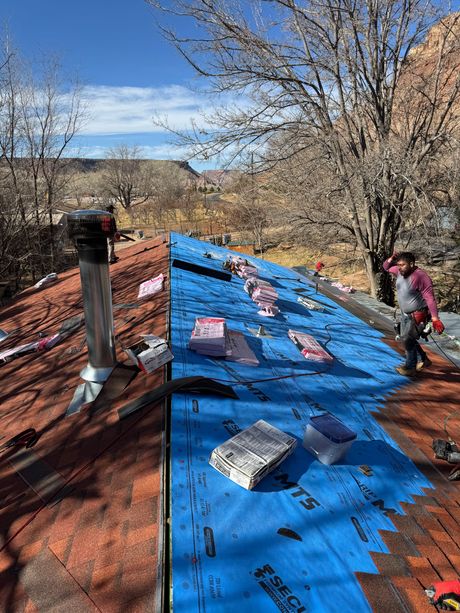 A man is standing on a roof with a blue tarp on it.
