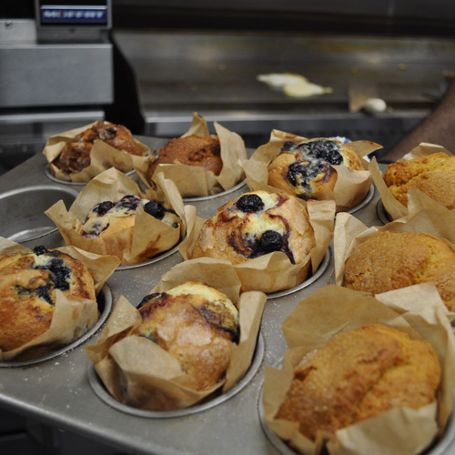 A tray of assorted freshly baked muffins in paper liners, featuring blueberry and golden brown varieties.