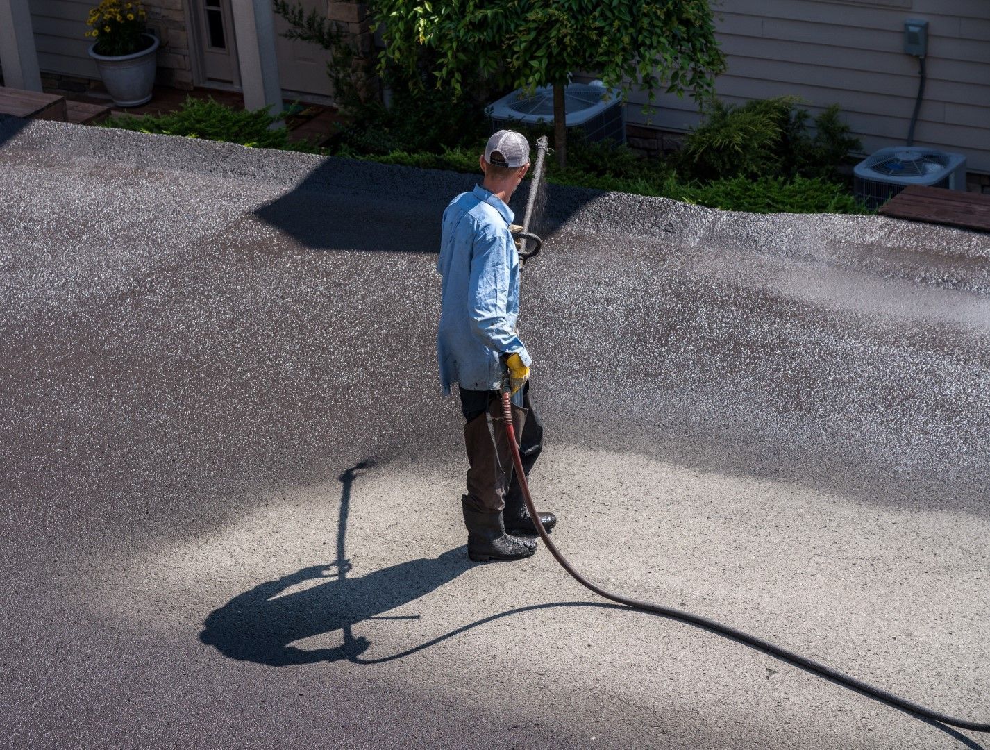 Man power washing a driveway, creating a light gray area on the dark asphalt.