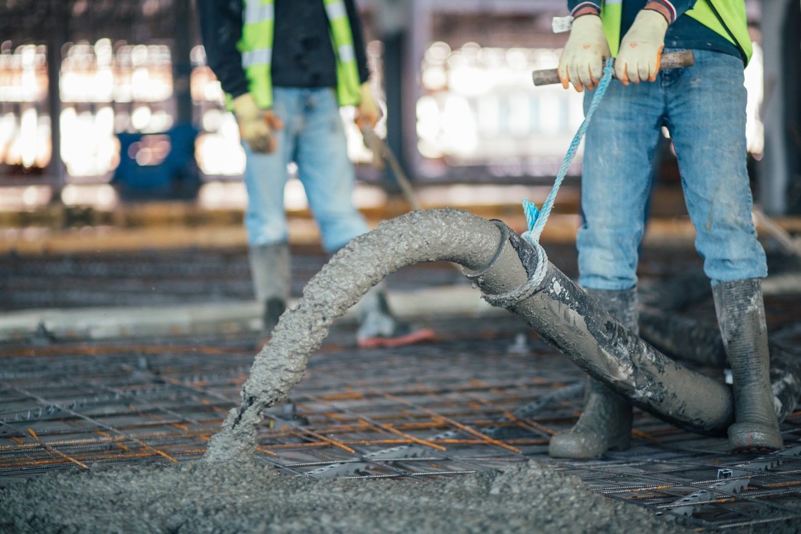Construction worker pouring concrete from a hose onto rebar on a building floor.