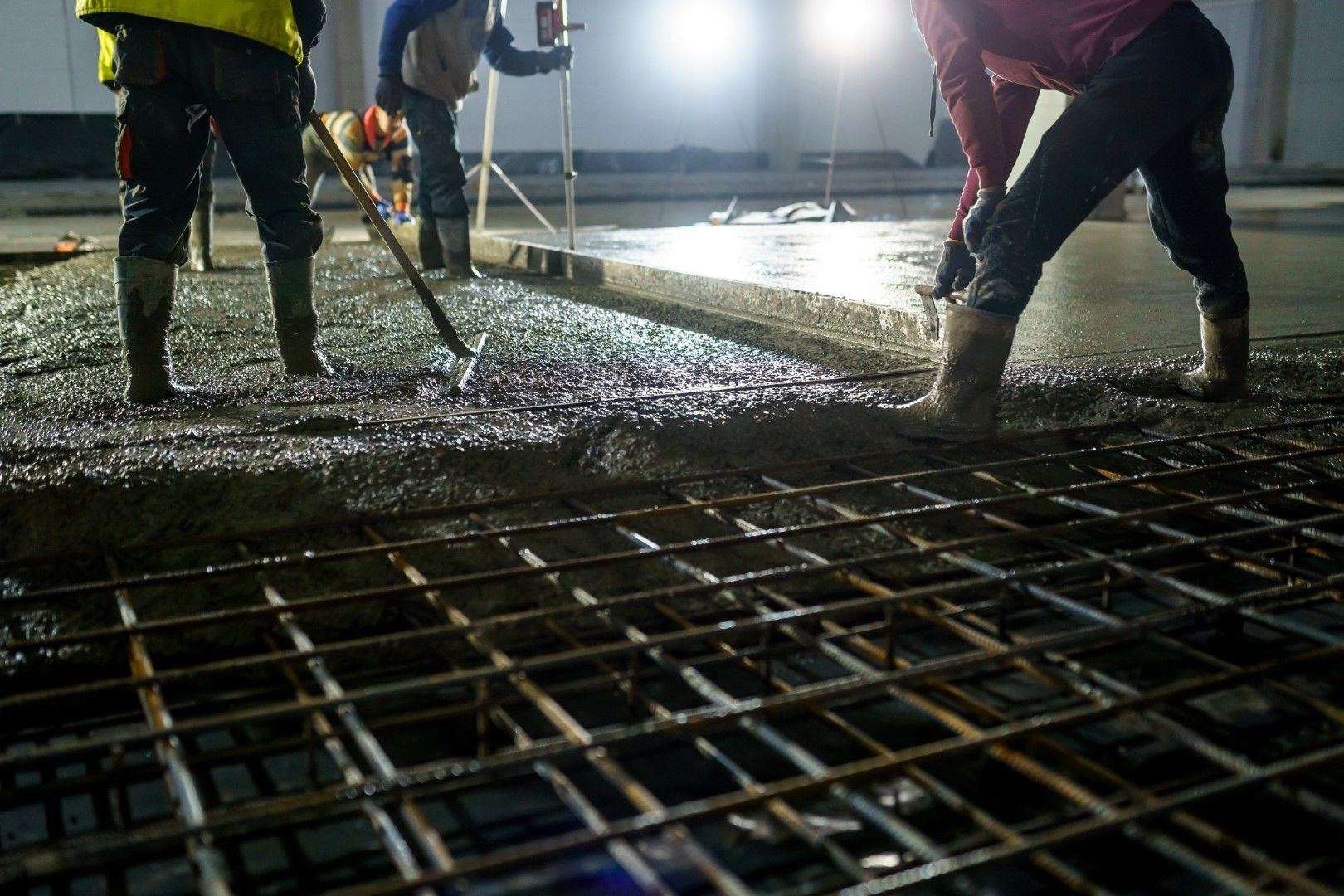 Construction workers pouring concrete over a steel rebar grid inside a building.